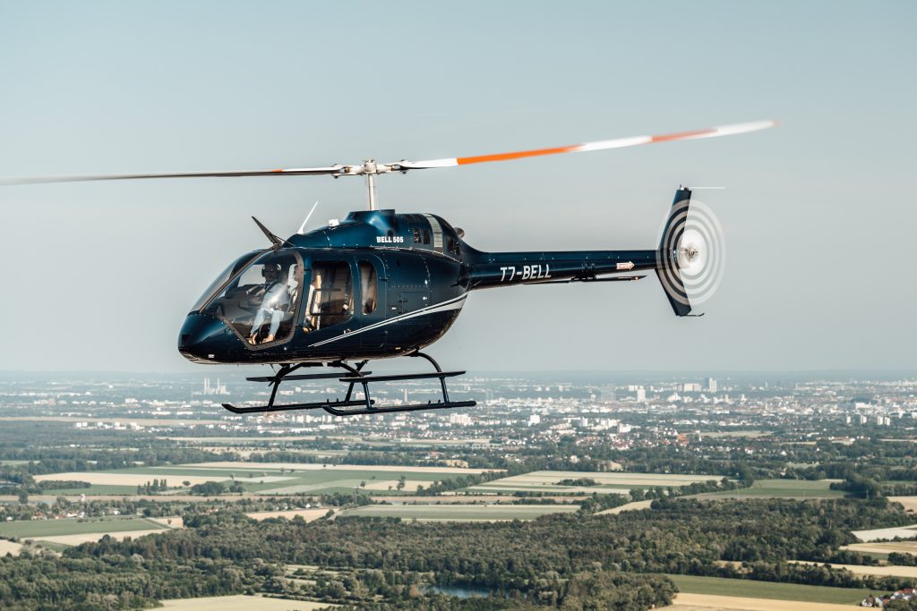 Bell 505 helicopter in flight over landscape, highlighting Helipaddy's aerial navigation services.