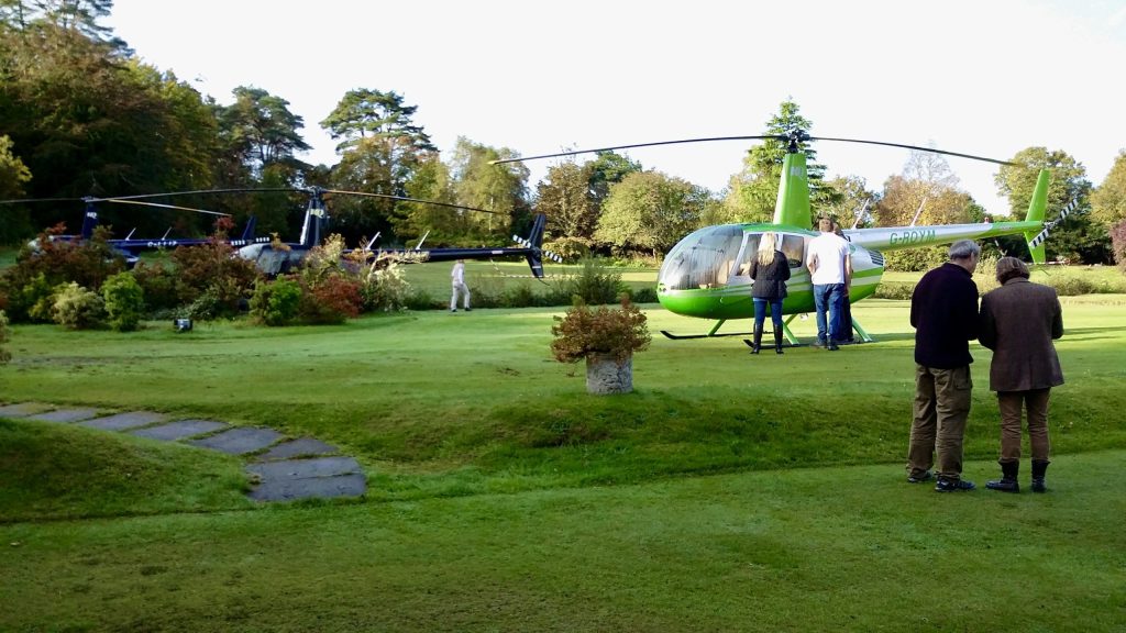 Helicopters on a grassy field with people, showcasing Helipaddy landing spot in a scenic area.