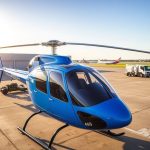 Blue helicopter on tarmac, clear sky, associated with Helipaddy landing info app.